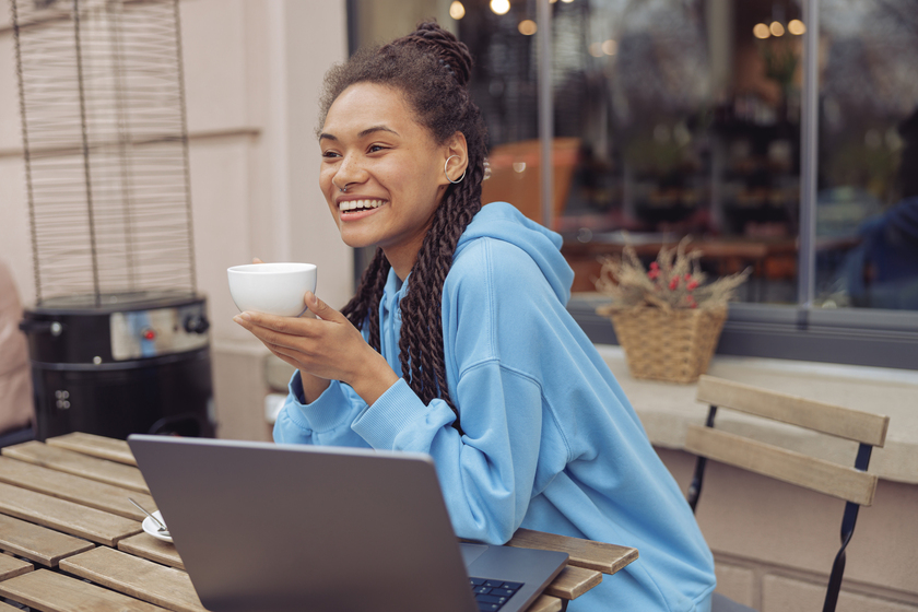 Beautiful young mixed-race cheerful woman with piercing holding coffee, smiling. Cafe terrace.